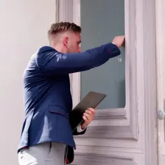 Mężczyzna w garniturze puka do drzwi, trzymając teczkę. Czy zastanawiasz się, ile komornik może zabrać z L4?