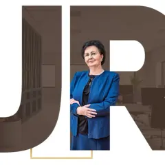 Kobieta w niebieskiej marynarce na tle liter JR i wnętrza biura.