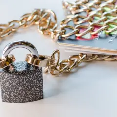Kłódka i złoty łańcuch oplatają karty kredytowe, symbolizując obawy o to, po jakim czasie komornik wchodzi na konto.
