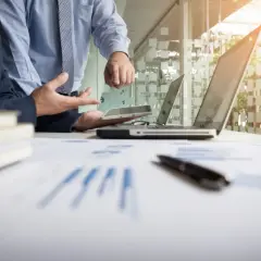 Dwóch mężczyzn w garniturach analizuje dokumenty i tablet w nowoczesnym biurze.