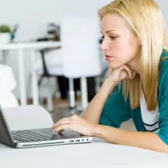 Kobieta z blond włosami pracuje na laptopie, analizując dokumenty dotyczące spłaconego komornika i kredytu hipotecznego.