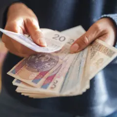 Dłonie trzymające stos polskich banknotów.