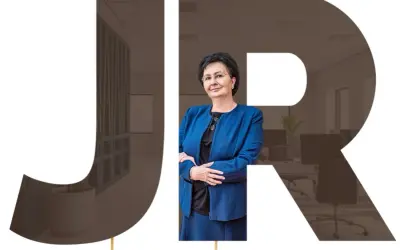 Kobieta w niebieskiej marynarce na tle liter JR i wnętrza biura.