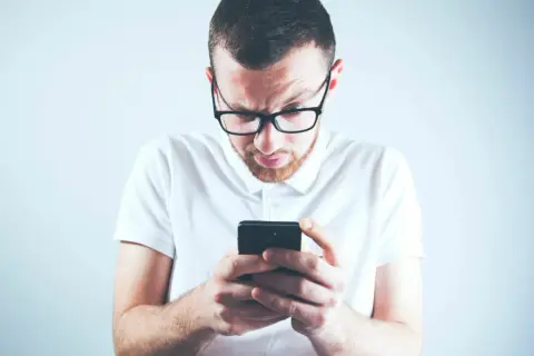 Zastanawiasz się, skąd firma windykacyjna ma Twój numer telefonu? Mężczyzna w okularach patrzy zdezorientowany na ekran smartfona.