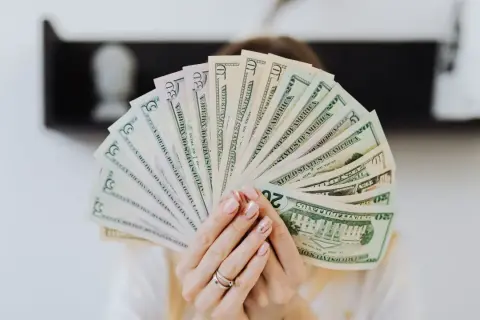 Dłonie trzymają wachlarz banknotów dolarowych. Szukasz firm, kto udziela finansowania firmom bez BIK?