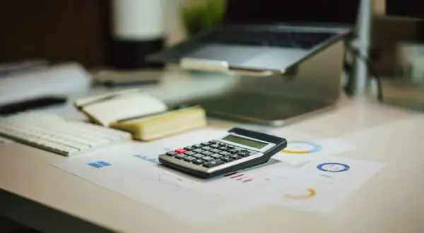 Kalkulator na biurku, obok laptopa i raportów. Czy wonga dzwoni do pracodawcy?