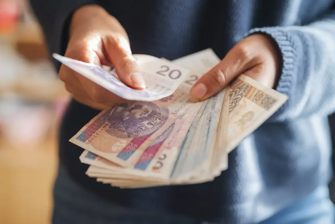 Dłonie trzymające stos polskich banknotów.
