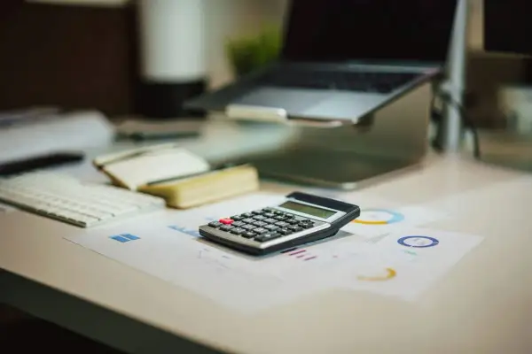 Kalkulator na biurku, obok laptopa i raportów. Czy wonga dzwoni do pracodawcy?