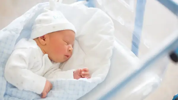 Śpiące noworodek w szpitalnym łóżeczku. Dowiedz się, jak wypełnić wniosek o becikowe, by zapewnić mu najlepszy start.
