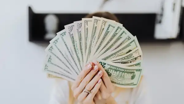 Dłonie trzymają wachlarz banknotów dolarowych. Szukasz firm, kto udziela finansowania firmom bez BIK?